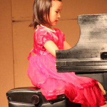 Young girl in pink dress playing piano on stage of 88 keys music academy spring festival