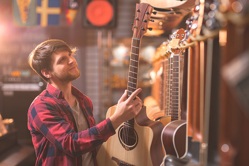 Young man in a red flannel choosing a guitar at a music store for how to pick the right guitar for you by 88 keys music academy