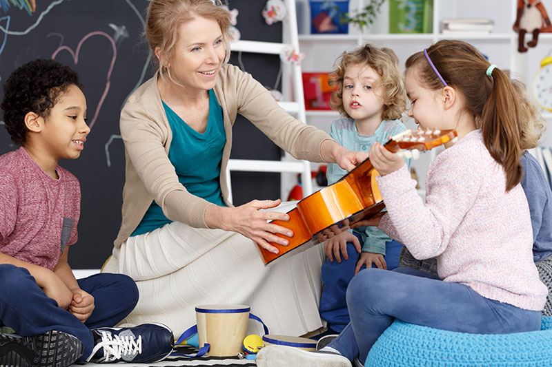 Woman guitar instructor in a classroom showing four students a guitar for how to pick the right guitar for you by 88 keys music academy